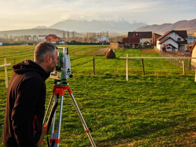 Surveyor conducting a boundary survey near residential homes to confirm property lines